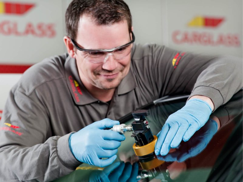 een carglass medewerker is aan het werk met de voorruit van een auto