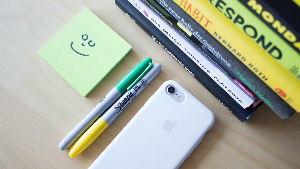 a telfone, a few markers, post its and some books on a desk