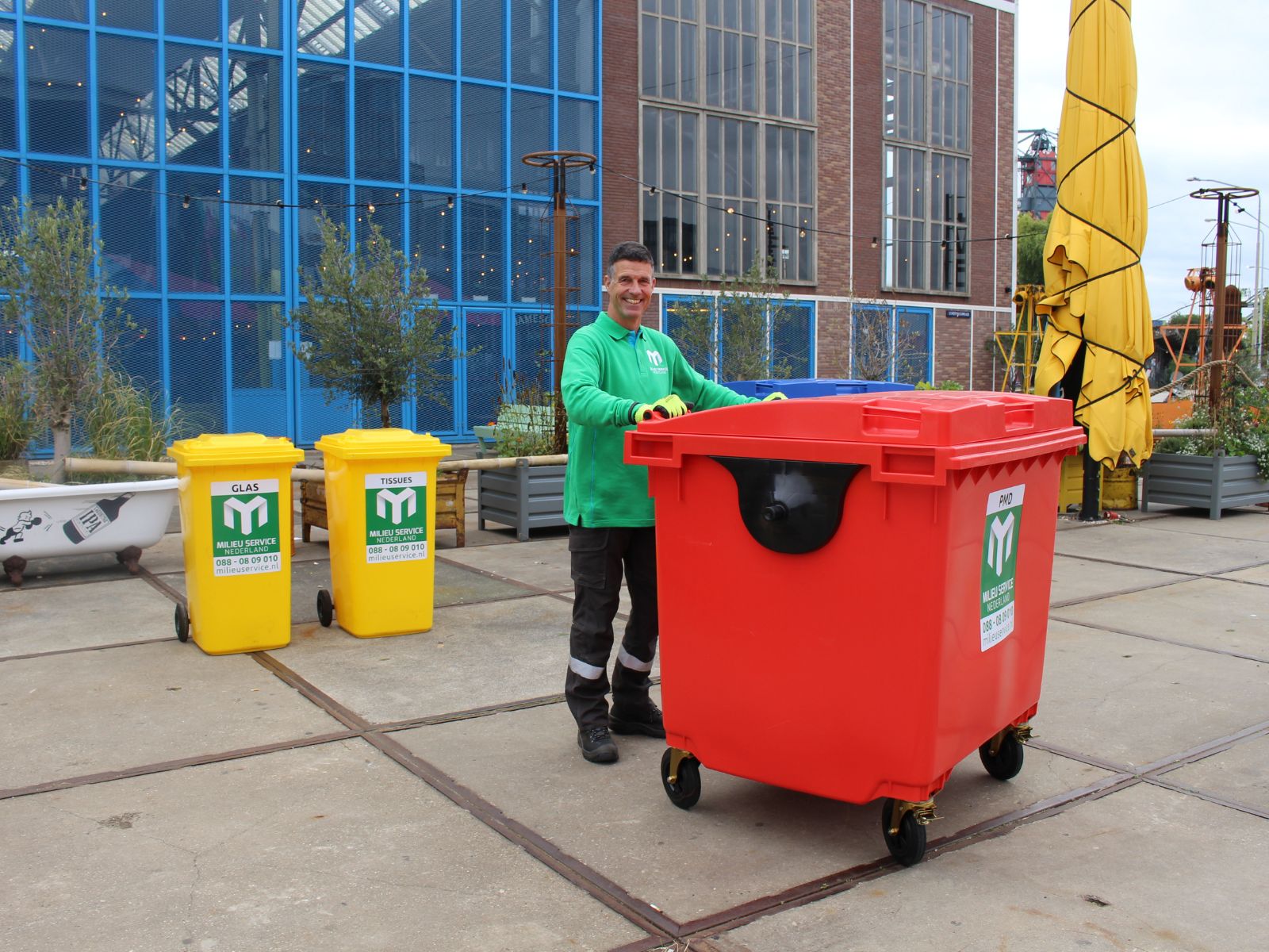 Man in groene trui met een rode container van milieuservice Nederland