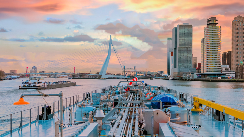 Een schip vaart de Rotterdamse Haven binnen, met zicht op de Erasmusbrug tijdens zonsondergang