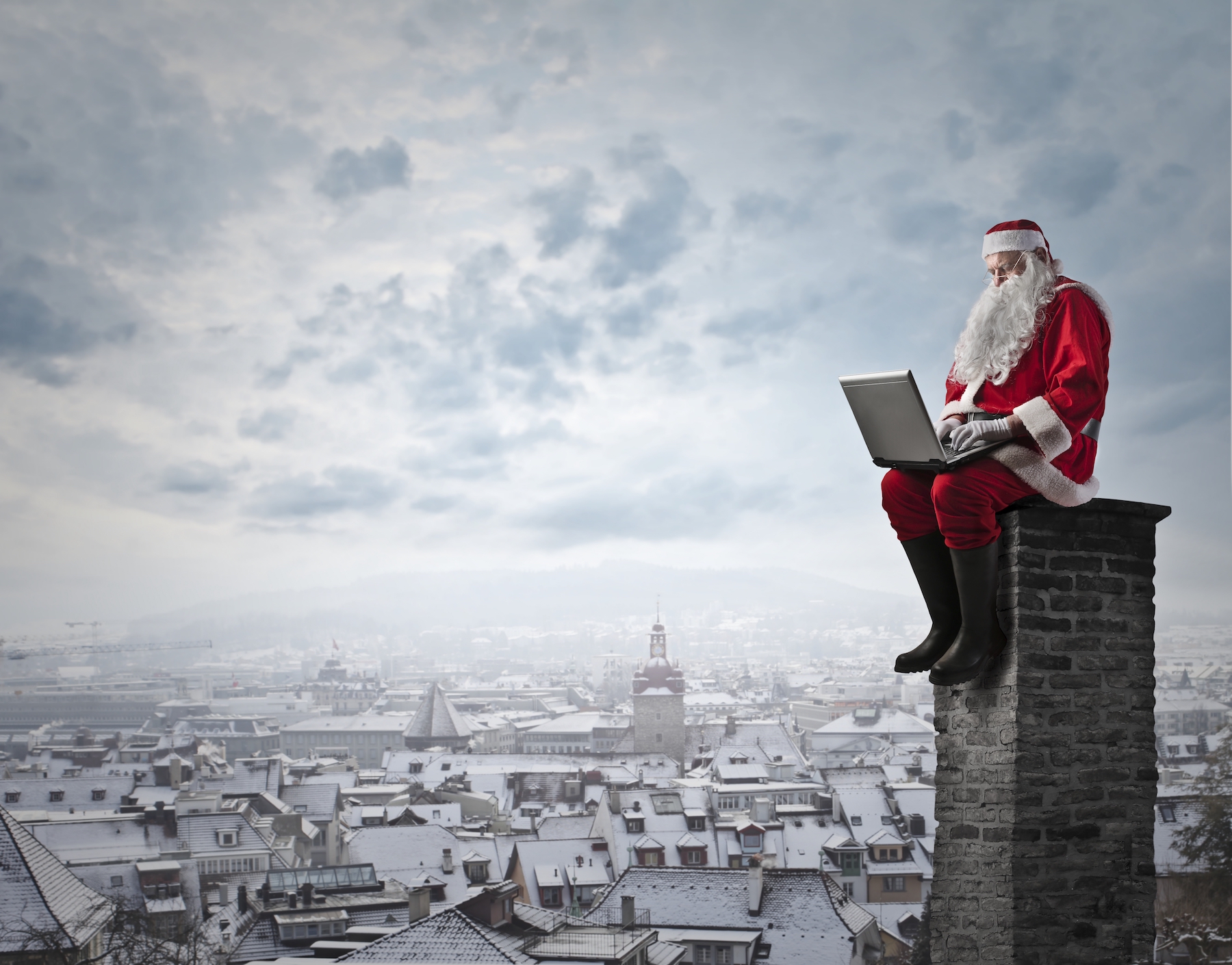 de kerstman zit op een schoorsteen met een laptop op schoot