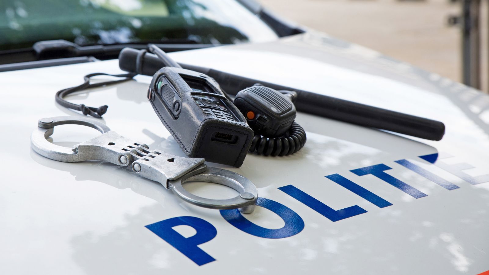 De motorkap van een politie auto waarop handboeien, een wapenstok en een walkietalkie liggen